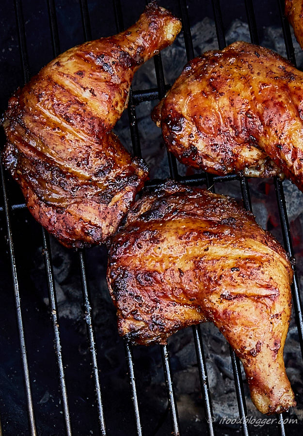 Deep golden brown chicken legs on a grill rack over red-hot charcoal.