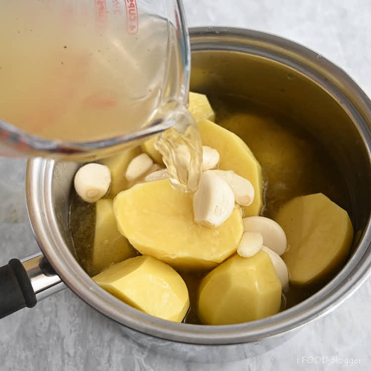 Pouring stock into a pan with potatoes and garlic.