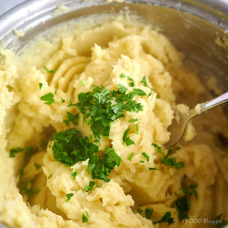 Adding cream and herbs to mashed potatoes in a bowl.