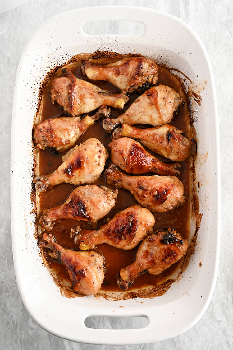 Baked chicken drumsticks, fully cooked, inside a rectangular white baking dish with sauce on the bottom.
