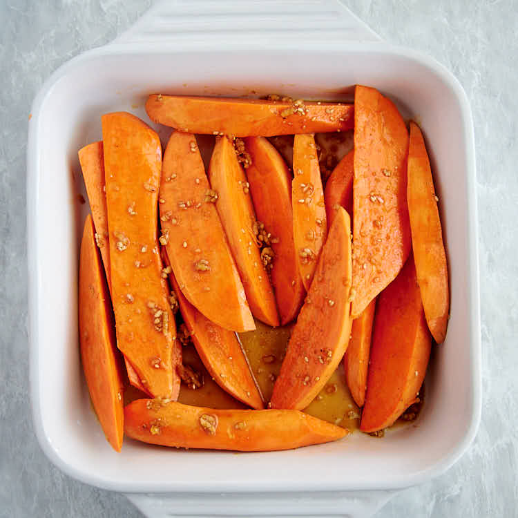 Sweet potatoes cut into wedges in a white baking dish.