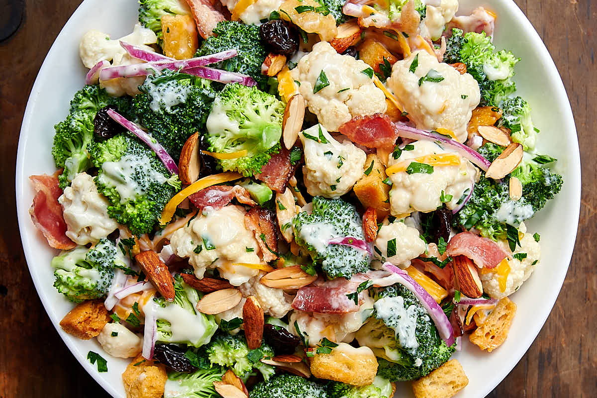 Broccoli and cauliflower salad (recipe) tossed with creamy dressing in white bowl.