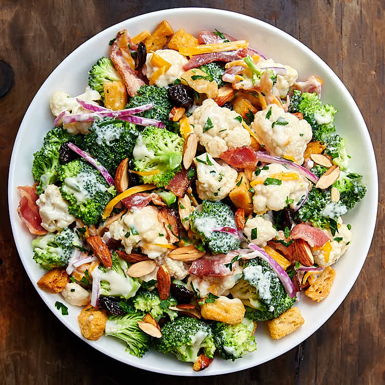 Broccoli and cauliflower salad (recipe) tossed with creamy dressing in white bowl.